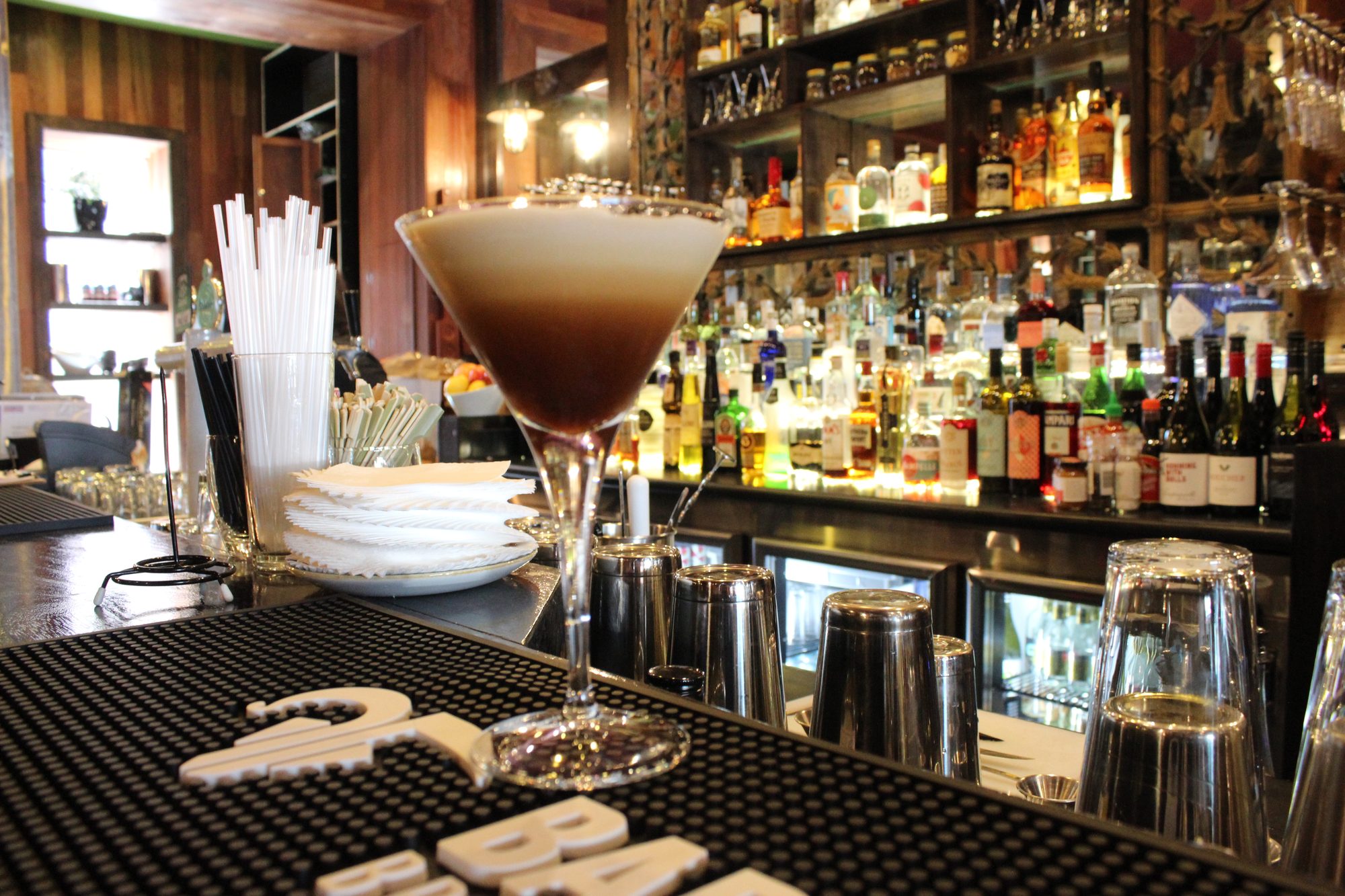 An espresso martini on the bar mat in front of the back bar